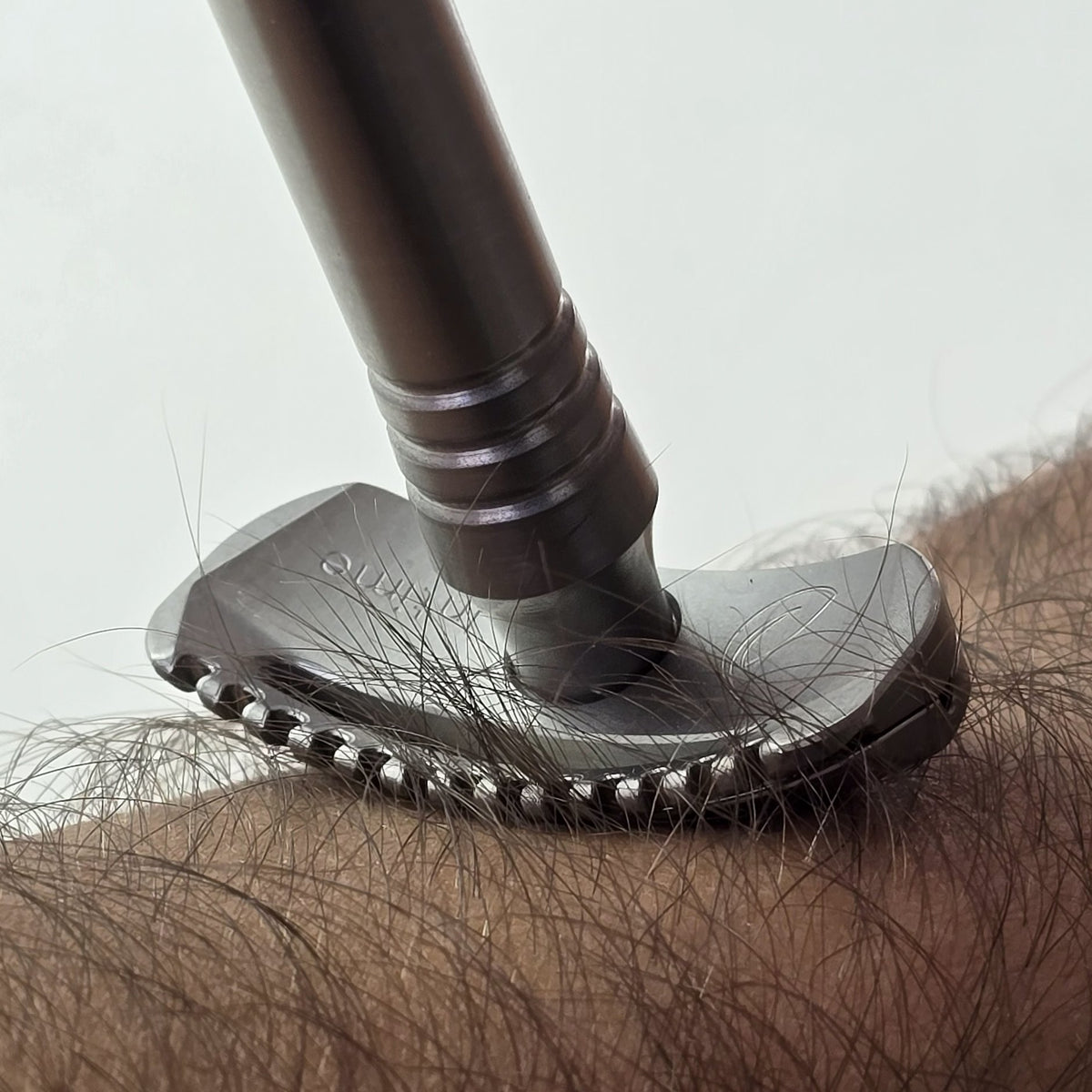 La tête de l’Intime posée sur un avant-bras : des poils longs passent entre les dents du peigne, devant la lame.